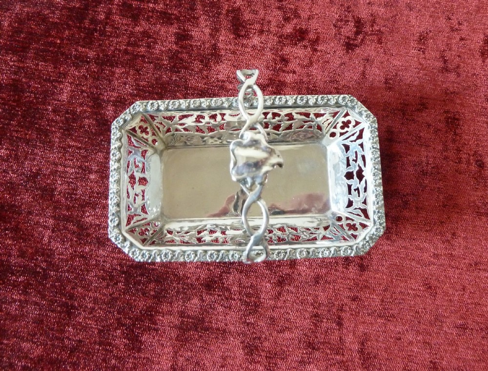 An Edwardian rectangular sterling silver basket with pierced fretwork sides, a looped overhead handle, and four cast feet. View II
