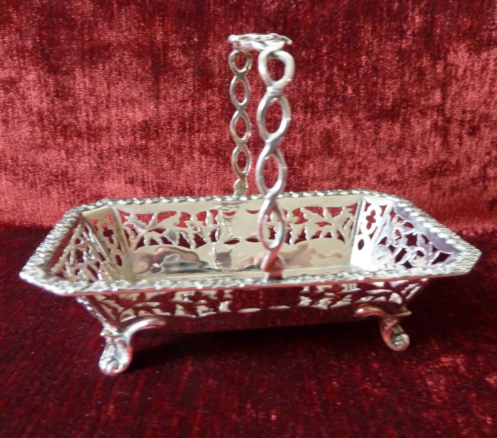 An Edwardian rectangular sterling silver basket with pierced fretwork sides, a looped overhead handle, and four cast feet. View III