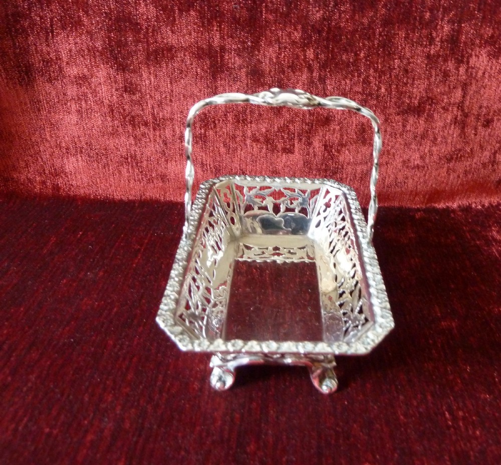 An Edwardian rectangular sterling silver basket with pierced fretwork sides, a looped overhead handle, and four cast feet. View IV