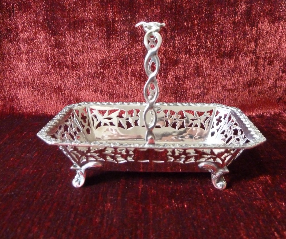 An Edwardian rectangular sterling silver basket with pierced fretwork sides, a looped overhead handle, and four cast feet. View V