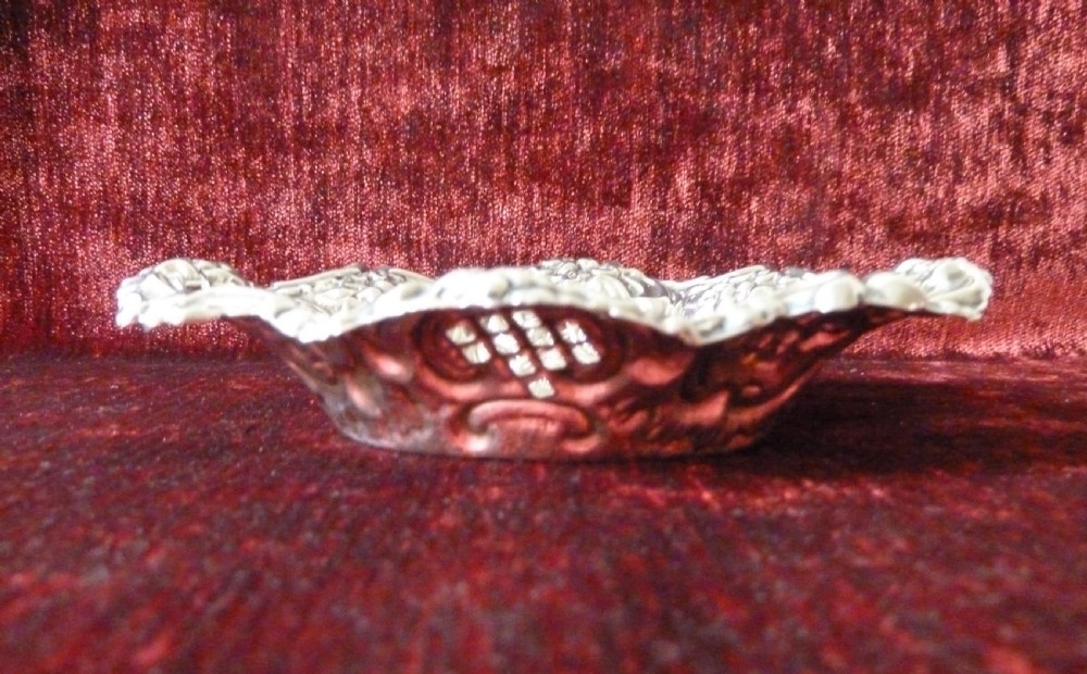 An oval Edwardian sterling silver pin dish featuring pierced lattice panels, repousse floral scroll borders, and a polished centre. View III