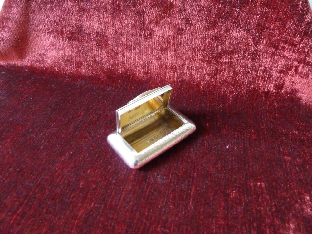 An open rectangular Georgian sterling silver snuff box displaying hallmark stamps on its gilded interior.