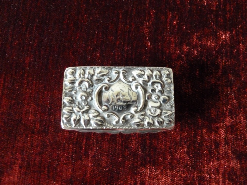 An open rectangular Victorian sterling silver snuff box displaying embossed scrollwork decoration and a gilded interior. View II