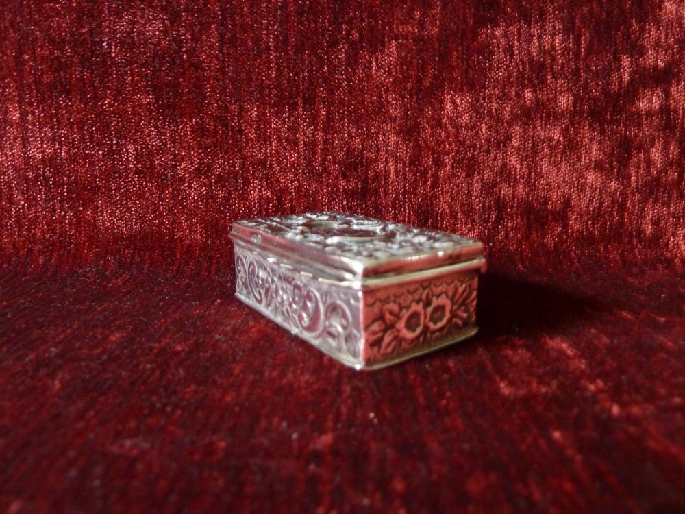 An open rectangular Victorian sterling silver snuff box displaying embossed scrollwork decoration and a gilded interior. View V