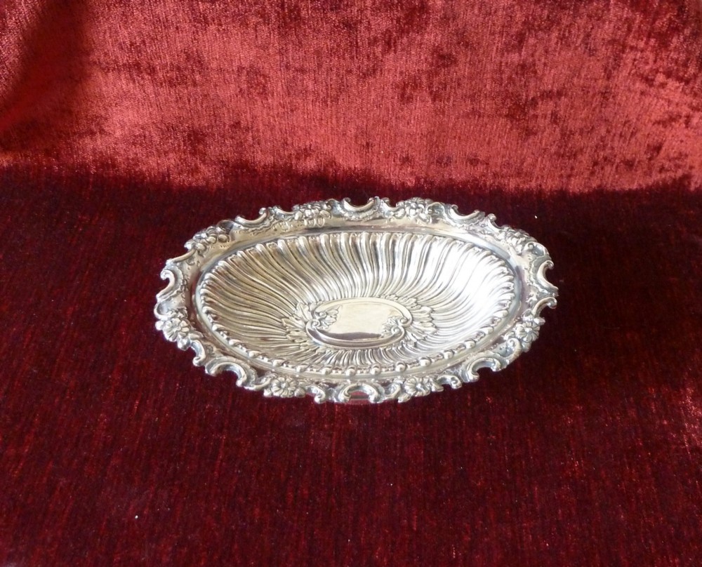 An oval Victorian sterling silver bonbon dish featuring a fluted body, scrollwork rim, and London hallmarks.
