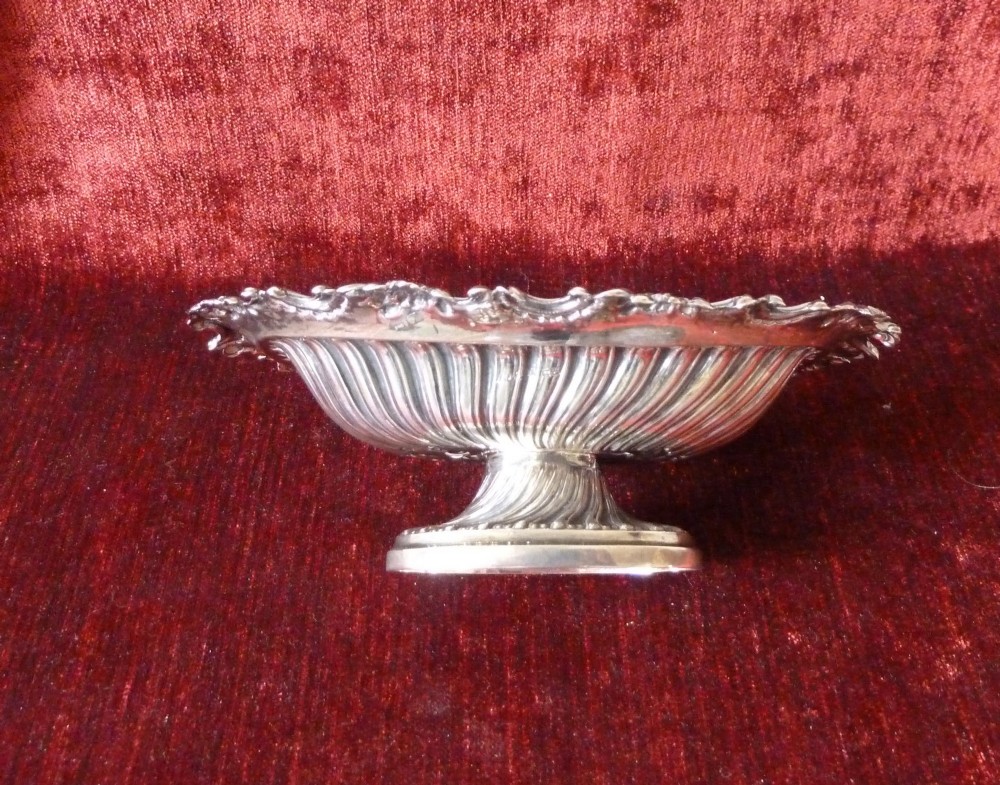 An oval Victorian sterling silver bonbon dish featuring a fluted body, scrollwork rim, and London hallmarks. View V