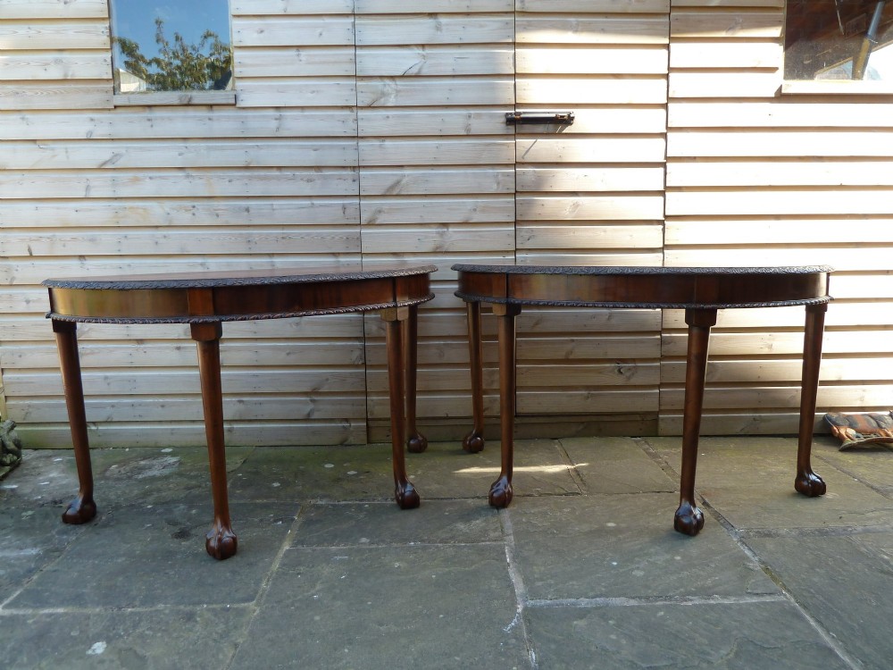 A pair of late 19th-century mahogany demilune console tables featuring carved aprons and cabriole legs with claw-and-ball feet.