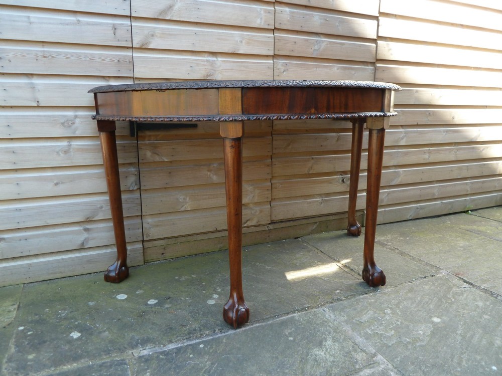 A pair of late 19th-century mahogany demilune console tables featuring carved aprons and cabriole legs with claw-and-ball feet. View X