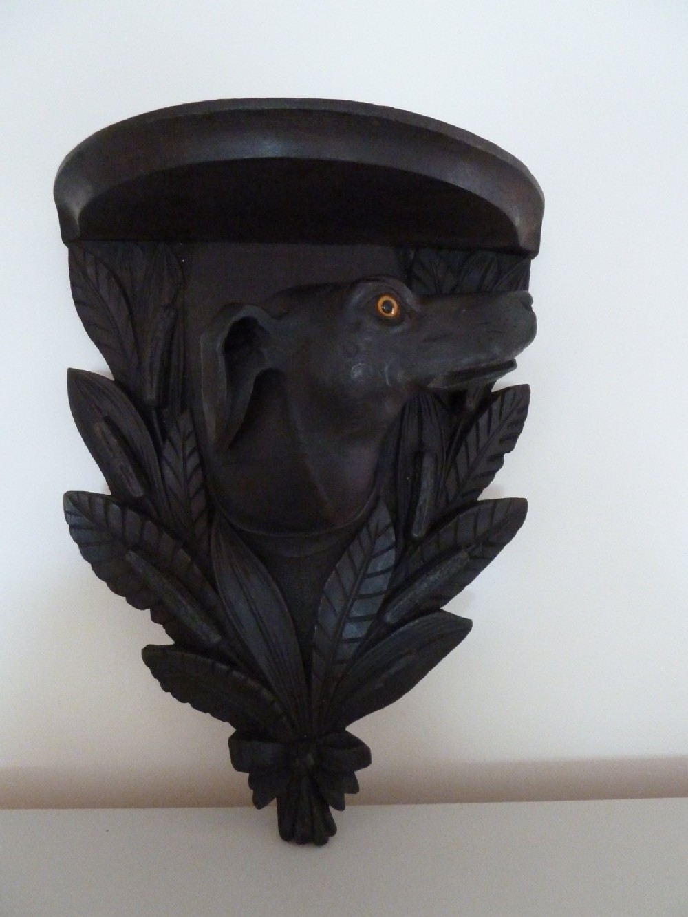 A dark brown hand-carved wooden wall bracket featuring a dog head surrounded by carved leaves below a small rounded shelf.