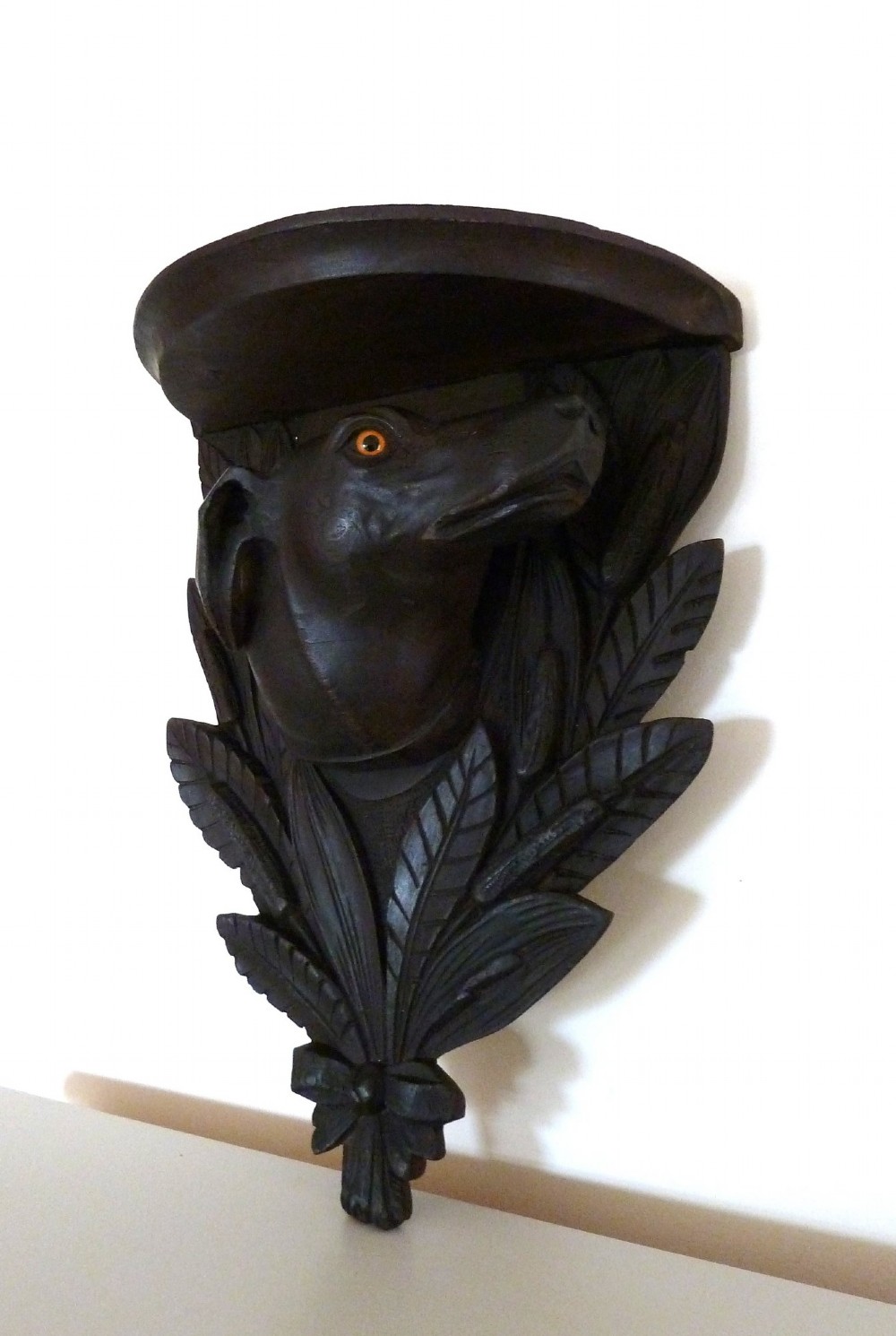 A dark brown hand-carved wooden wall bracket featuring a dog head surrounded by carved leaves below a small rounded shelf. View III