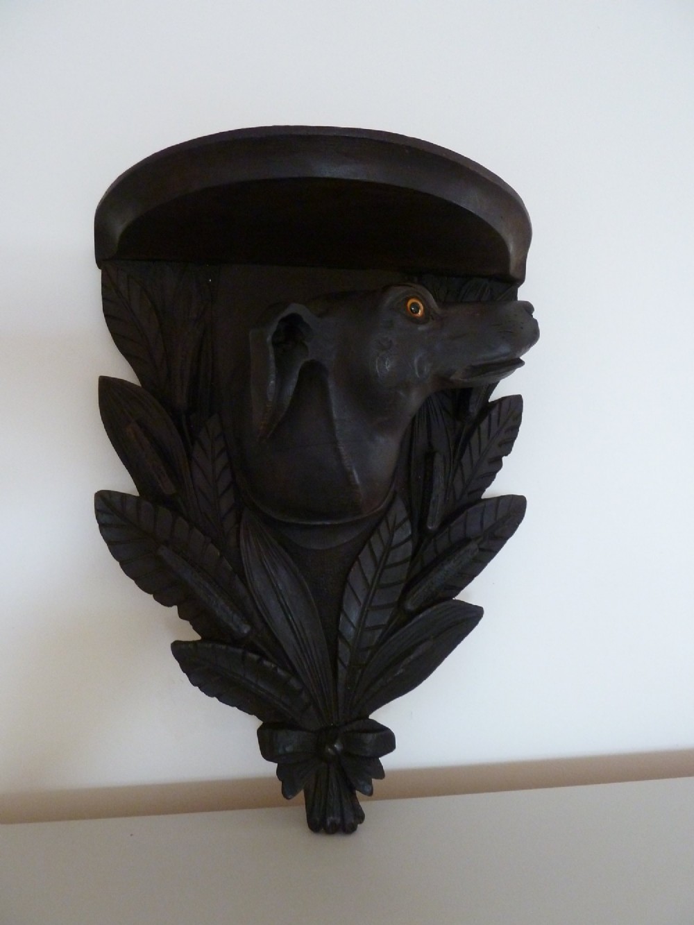 A dark brown hand-carved wooden wall bracket featuring a dog head surrounded by carved leaves below a small rounded shelf. View IV