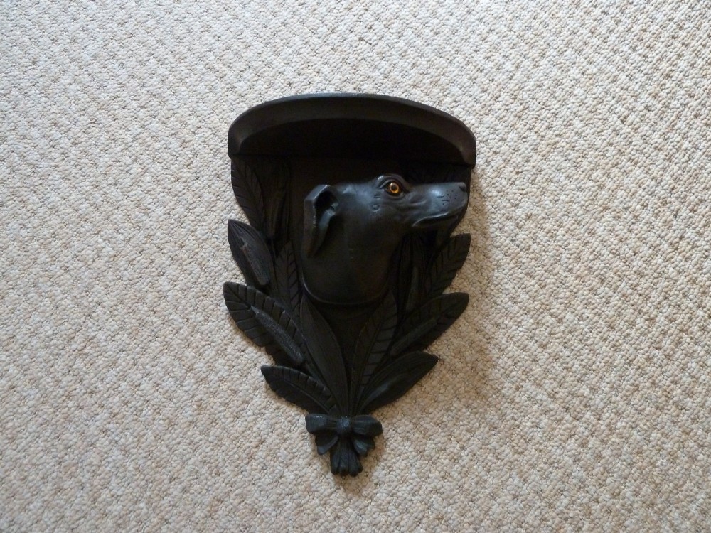 A dark brown hand-carved wooden wall bracket featuring a dog head surrounded by carved leaves below a small rounded shelf. View IX