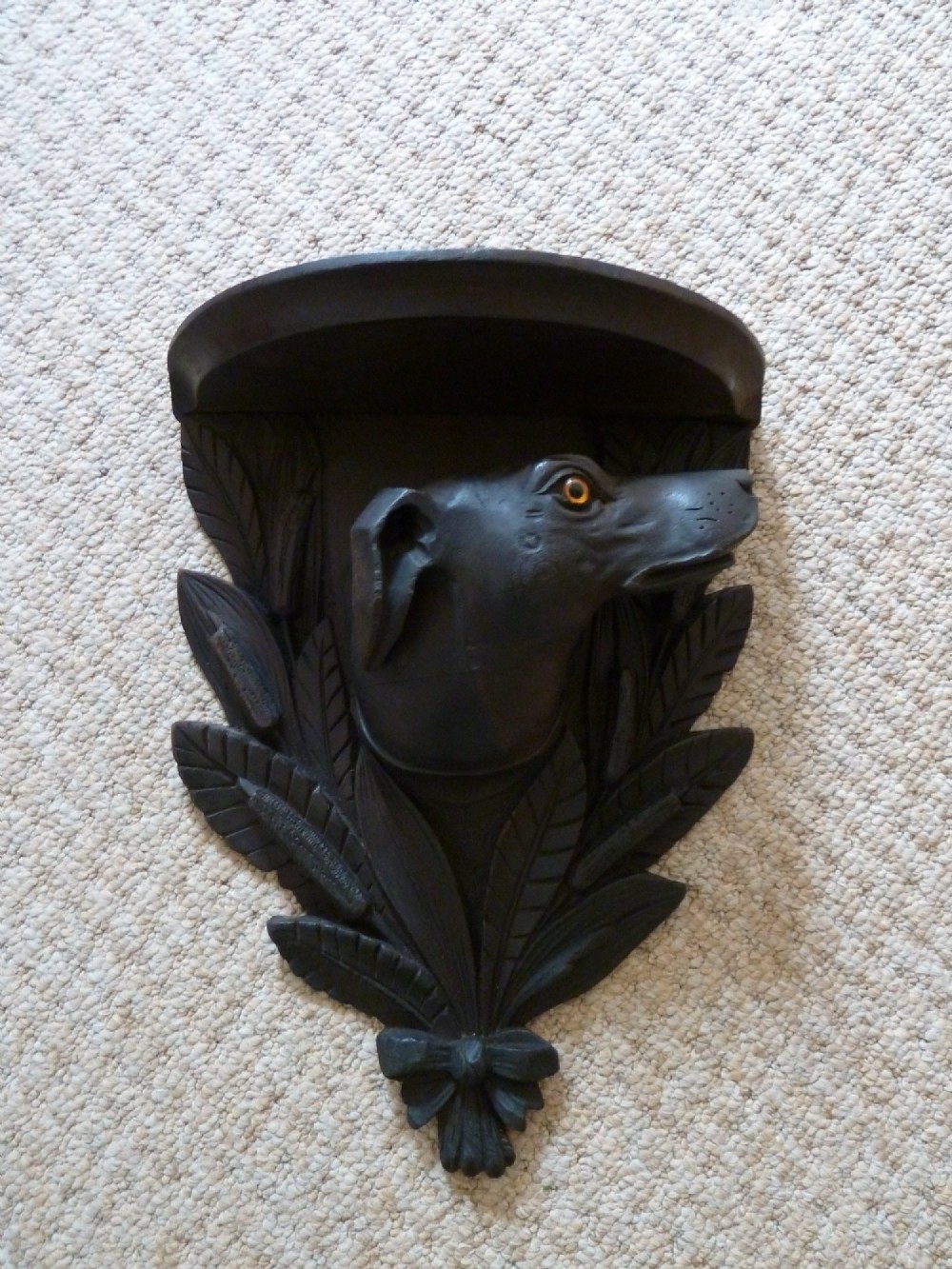 A dark brown hand-carved wooden wall bracket featuring a dog head surrounded by carved leaves below a small rounded shelf. View VIII