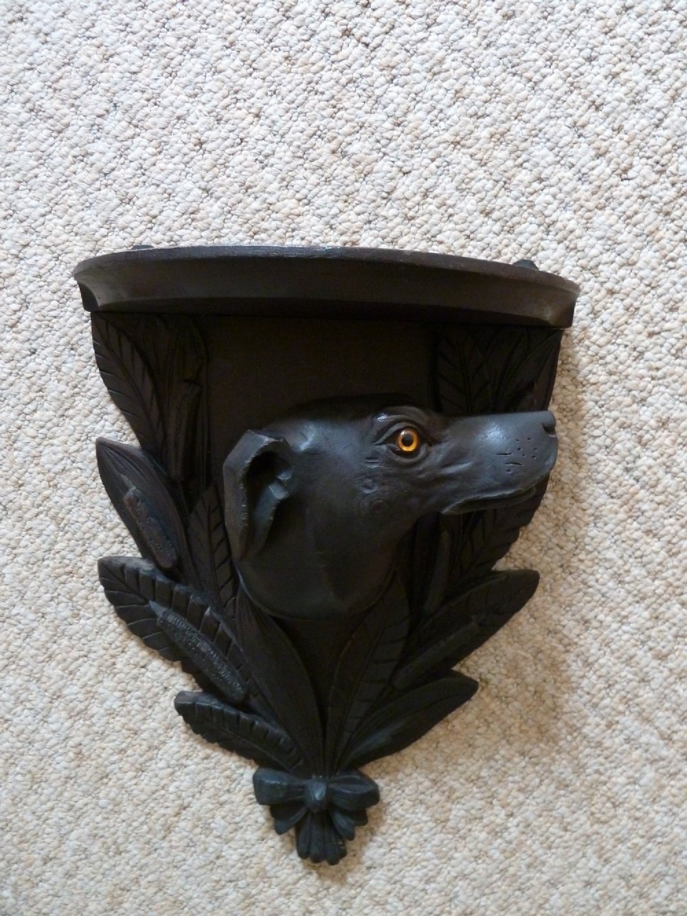 A dark brown hand-carved wooden wall bracket featuring a dog head surrounded by carved leaves below a small rounded shelf. View XI