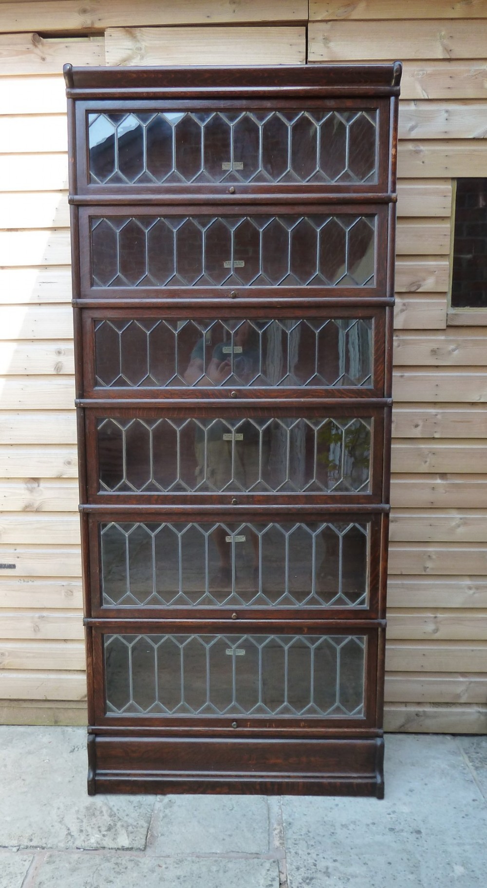 A tall dark oak Globe Wernicke sectional bookcase featuring six glazed tiers with geometric leaded glass doors and brass handles.