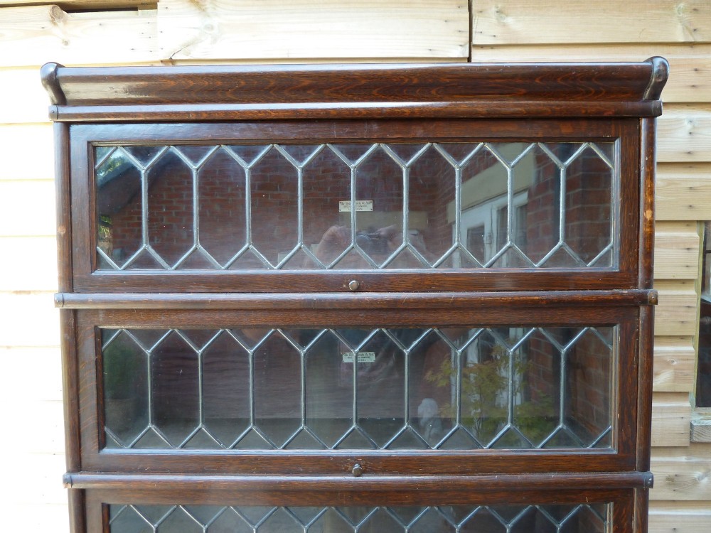 A tall dark oak Globe Wernicke sectional bookcase featuring six glazed tiers with geometric leaded glass doors and brass handles. View V