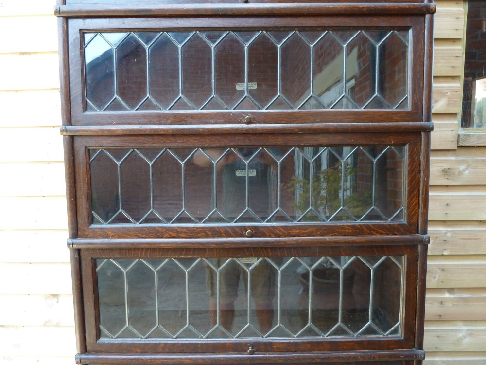 A tall dark oak Globe Wernicke sectional bookcase featuring six glazed tiers with geometric leaded glass doors and brass handles. View VI
