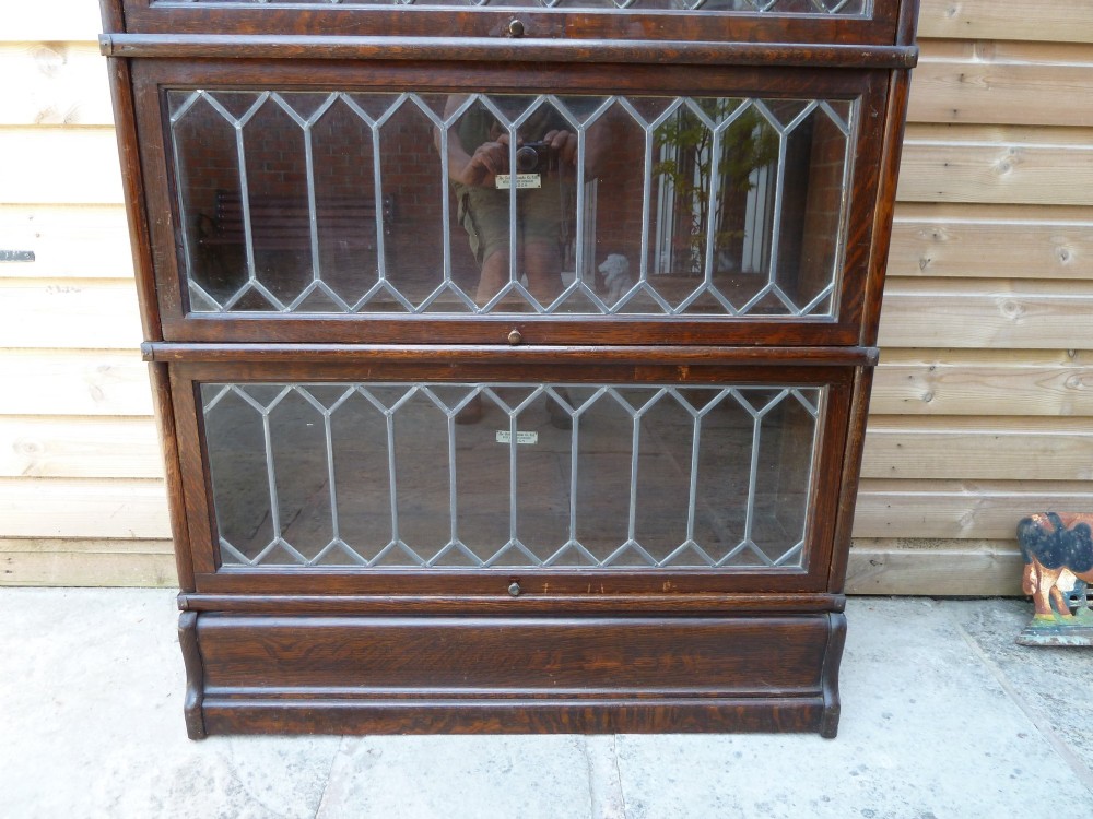 A tall dark oak Globe Wernicke sectional bookcase featuring six glazed tiers with geometric leaded glass doors and brass handles. View VII