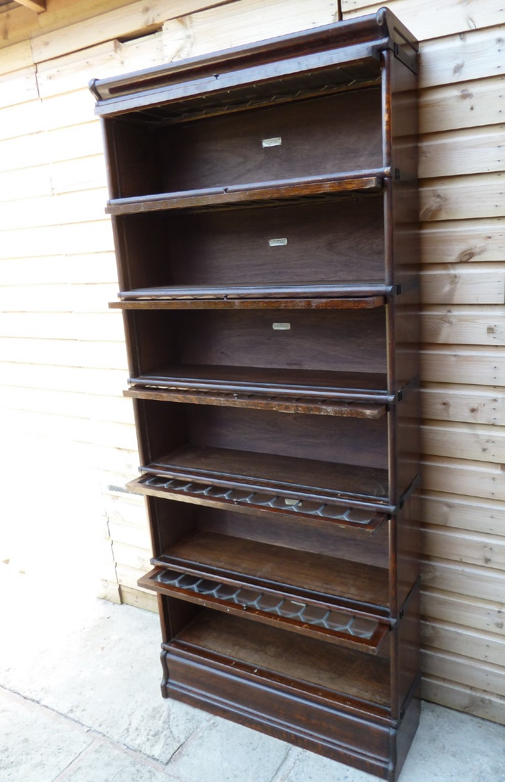 A tall dark oak Globe Wernicke sectional bookcase featuring six glazed tiers with geometric leaded glass doors and brass handles. View XI
