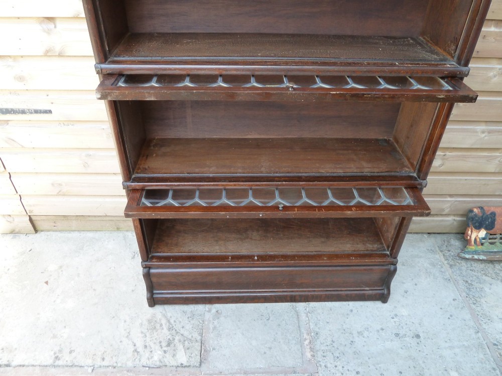 A tall dark oak Globe Wernicke sectional bookcase featuring six glazed tiers with geometric leaded glass doors and brass handles. View XII