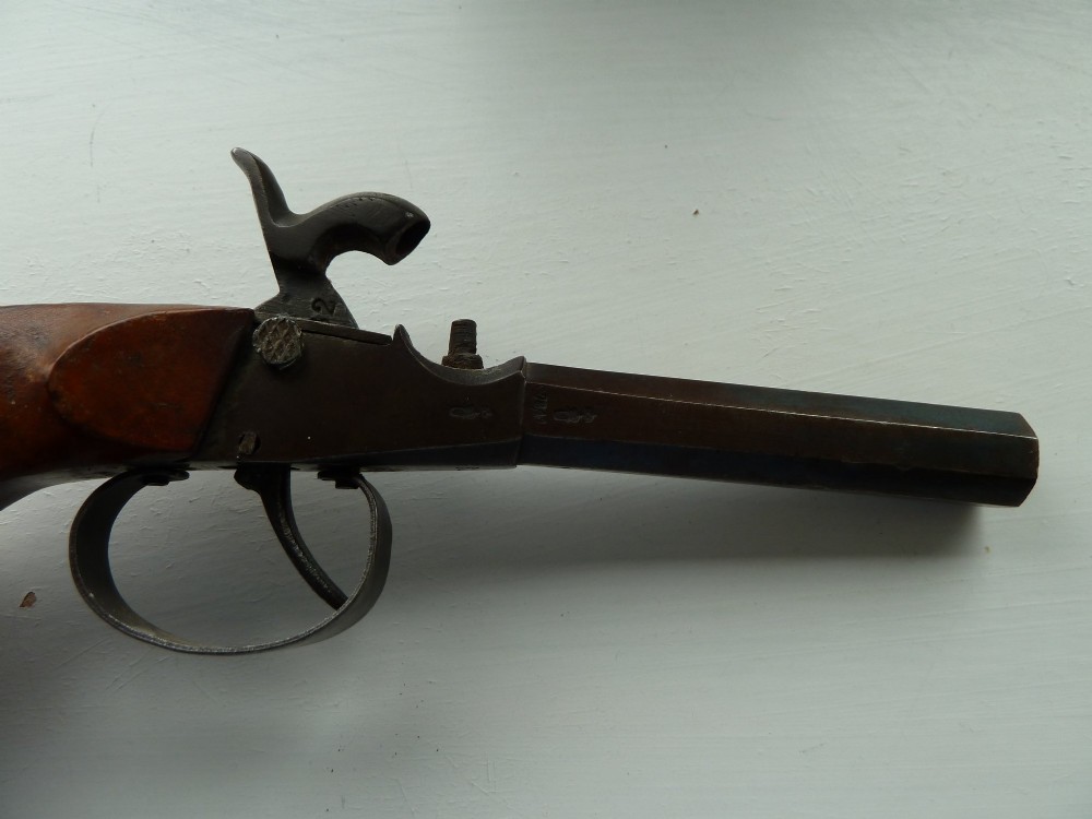 A 19th-century percussion pocket pistol featuring an octagonal steel barrel, iron trigger guard, and smooth curved wooden grip. View VI