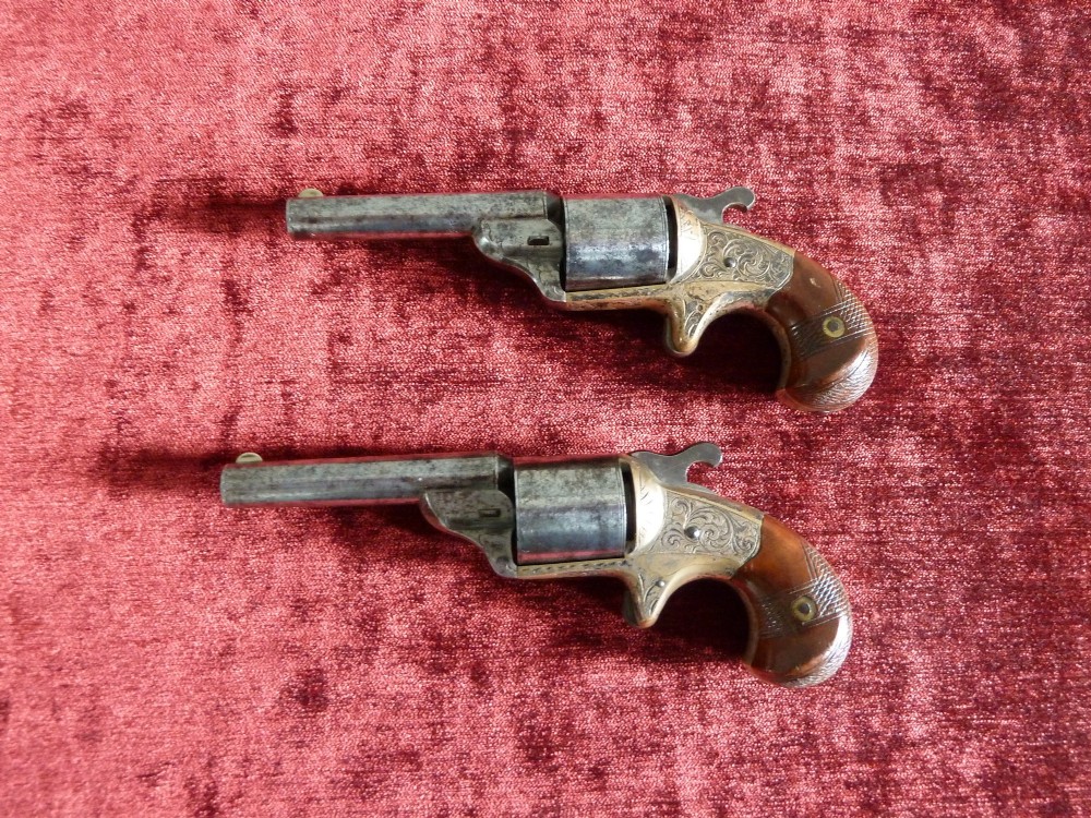 A pair of 19th-century American rimfire pocket revolvers featuring engraved metal frames, cylindrical barrels, and smooth wood grips. View II