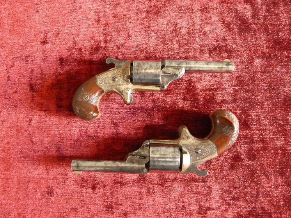 A pair of 19th-century American rimfire pocket revolvers featuring engraved metal frames, cylindrical barrels, and smooth wood grips. View III