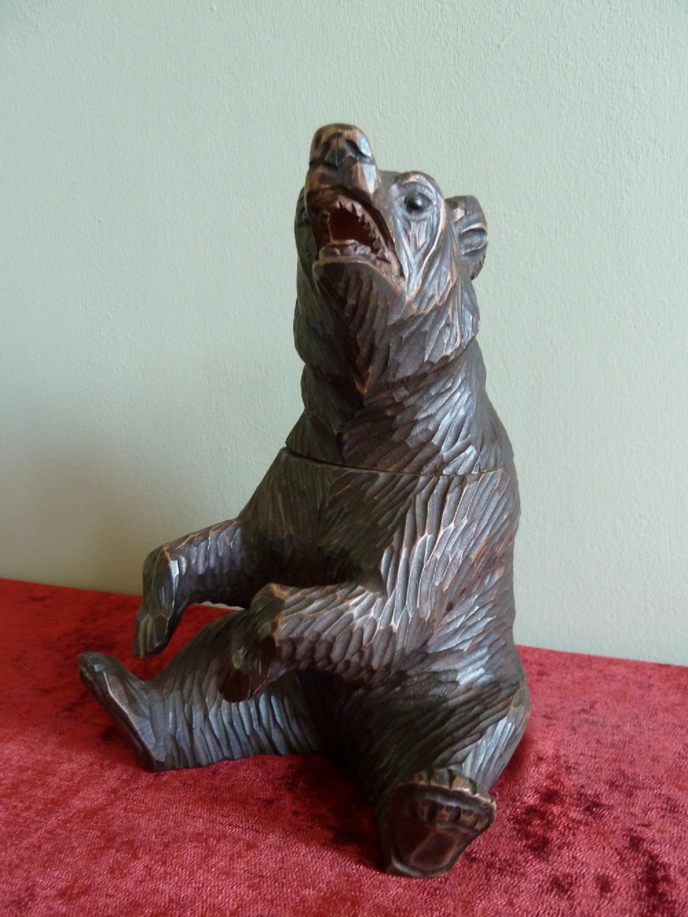 A carved dark brown wooden Black Forest bear depicted in a seated position with open jaws, featuring a removable head function.