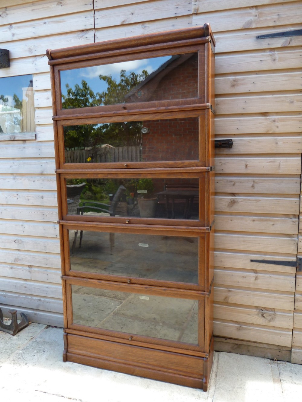 A five-tier golden oak Globe Wernicke modular bookcase featuring glazed up-and-over doors and brass knob handles.