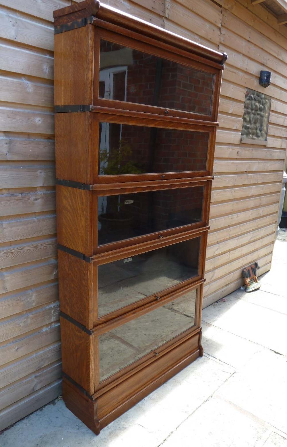 A five-tier golden oak Globe Wernicke modular bookcase featuring glazed up-and-over doors and brass knob handles. View II