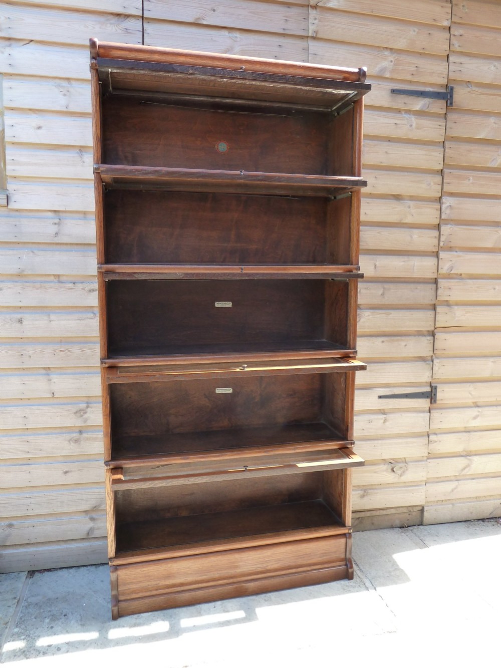 A five-tier golden oak Globe Wernicke modular bookcase featuring glazed up-and-over doors and brass knob handles. View VI