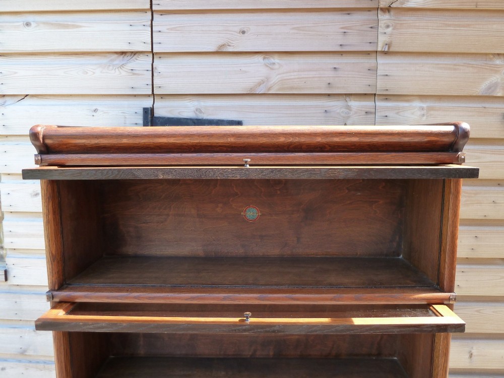 A five-tier golden oak Globe Wernicke modular bookcase featuring glazed up-and-over doors and brass knob handles. View X