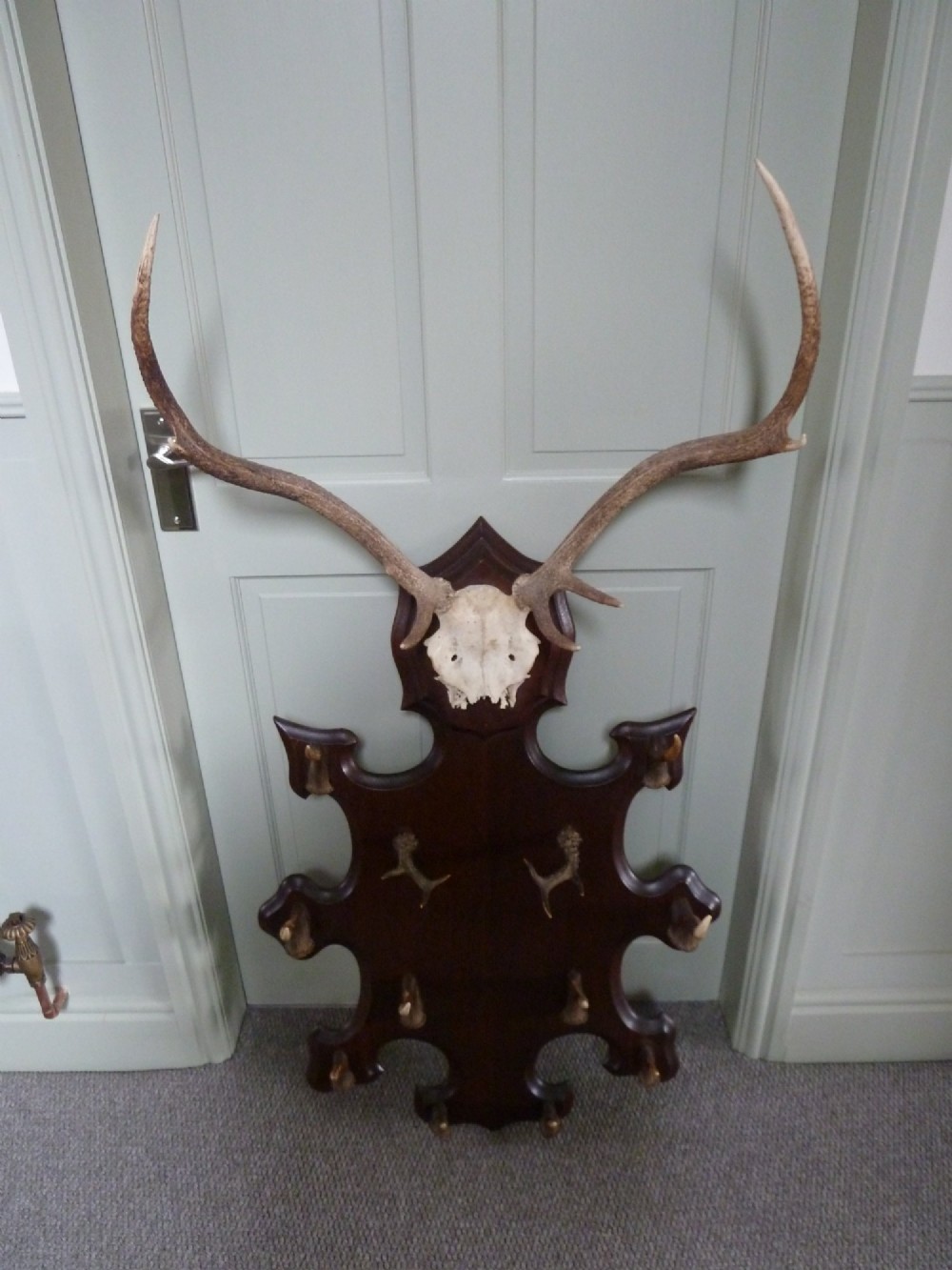 A dark carved oak backboard mounted with a stag skull and multiple small antler hooks for hanging coats. View VI