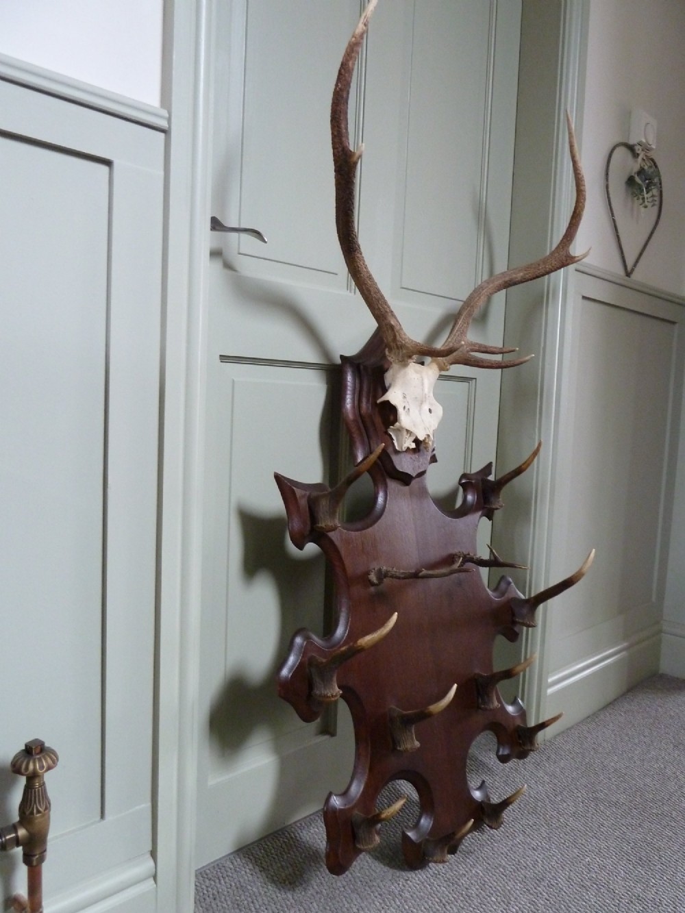 A dark carved oak backboard mounted with a stag skull and multiple small antler hooks for hanging coats. View VIII