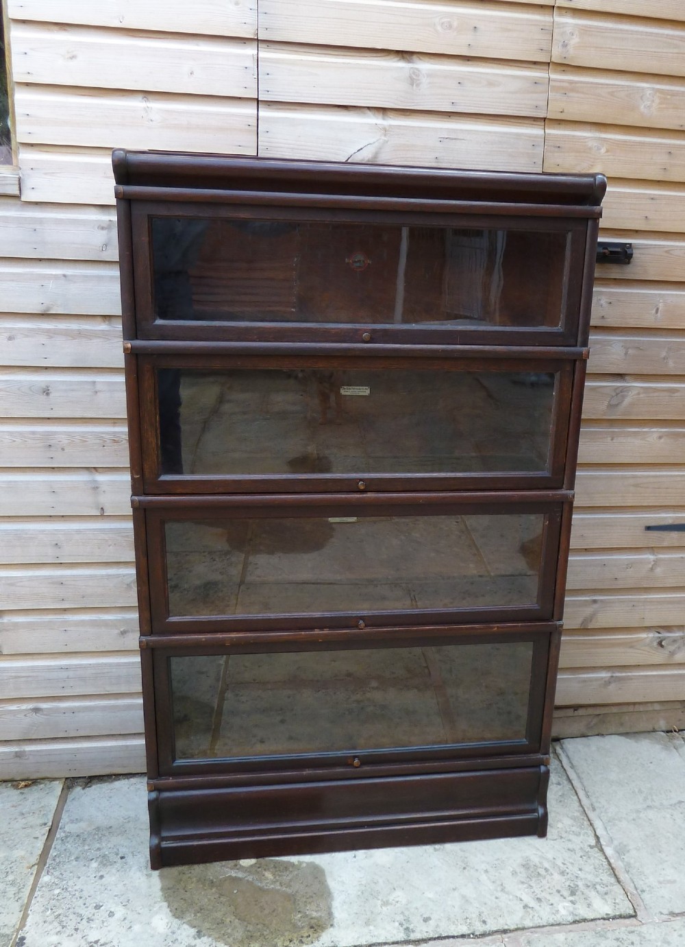 A four-tier dark oak Globe Wernicke sectional bookcase featuring glazed lift-up doors and a plinth base.