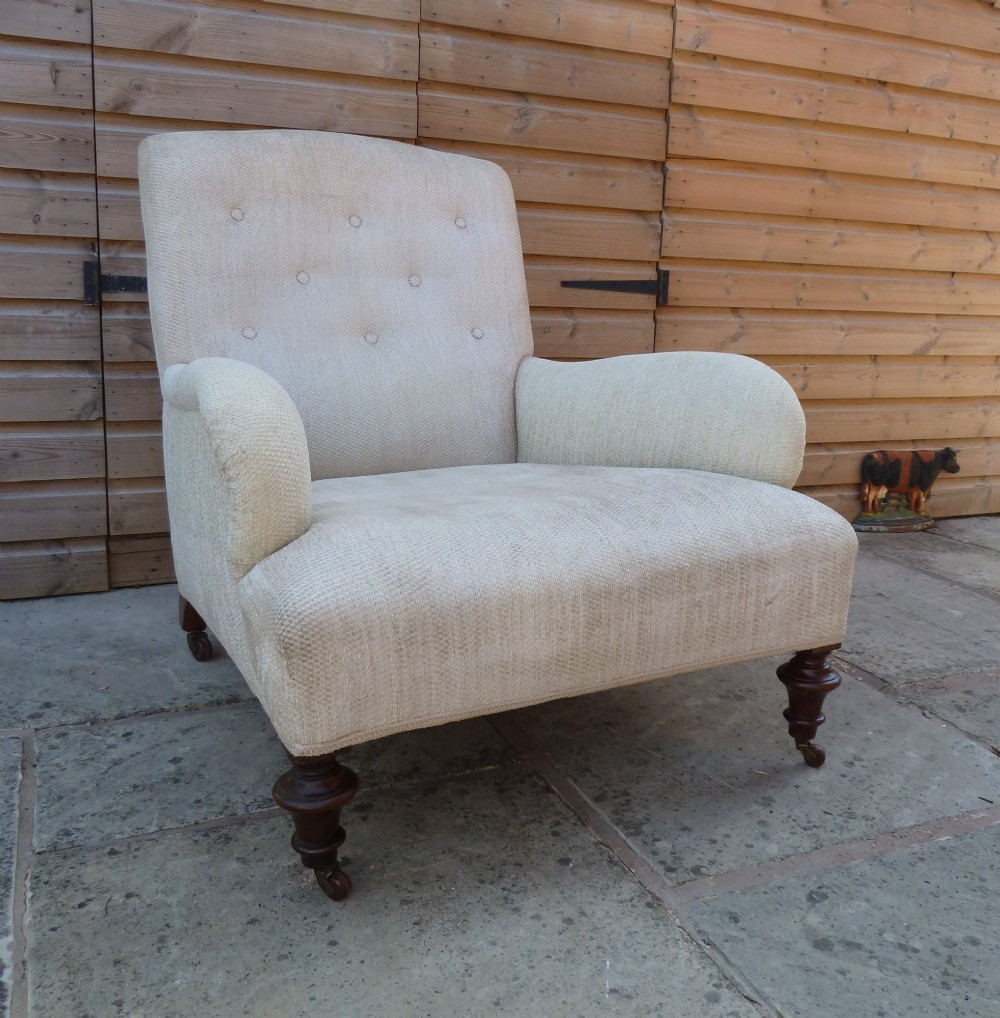 A low-slung, cream fabric upholstered armchair with a buttoned backrest, padded scroll arms, and dark turned legs on castors. View III