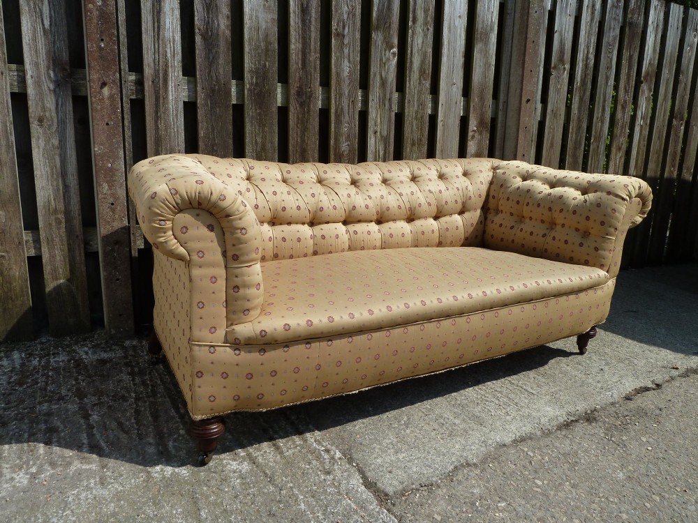 A Victorian button-back sofa upholstered in a gold and beige patterned fabric, featuring scrolled arms and turned wooden legs on brass castors. View II