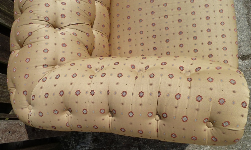 A Victorian button-back sofa upholstered in a gold and beige patterned fabric, featuring scrolled arms and turned wooden legs on brass castors. View V