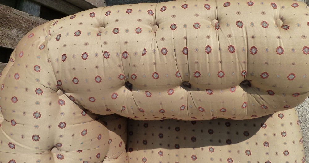 A Victorian button-back sofa upholstered in a gold and beige patterned fabric, featuring scrolled arms and turned wooden legs on brass castors. View VI