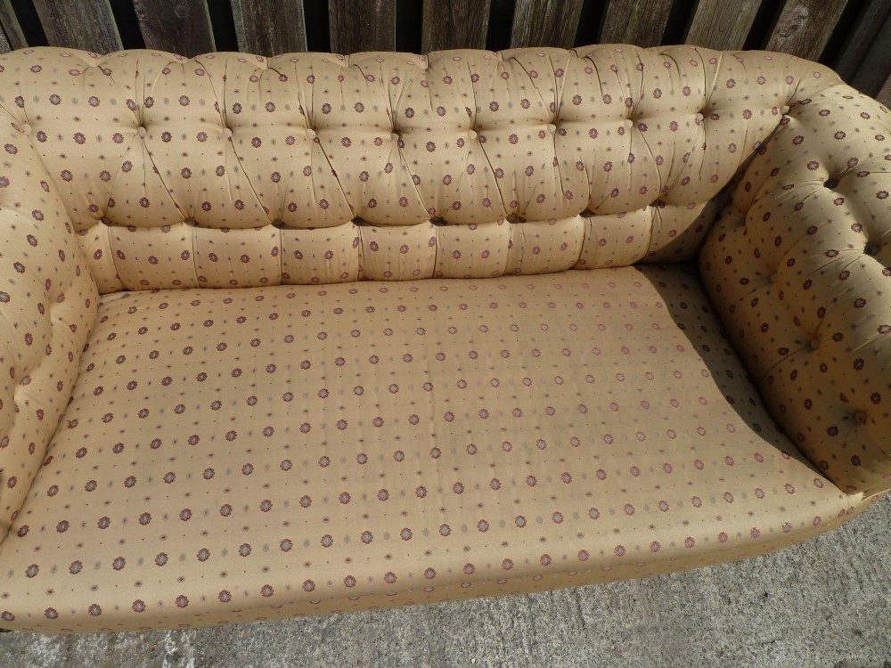 A Victorian button-back sofa upholstered in a gold and beige patterned fabric, featuring scrolled arms and turned wooden legs on brass castors. View VII