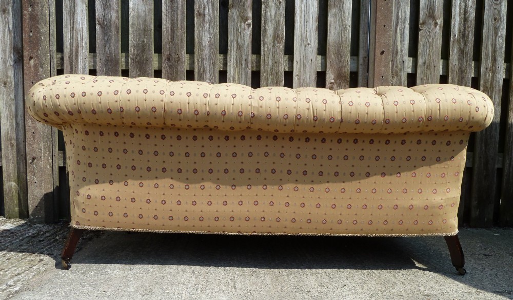 A Victorian button-back sofa upholstered in a gold and beige patterned fabric, featuring scrolled arms and turned wooden legs on brass castors. View VIII
