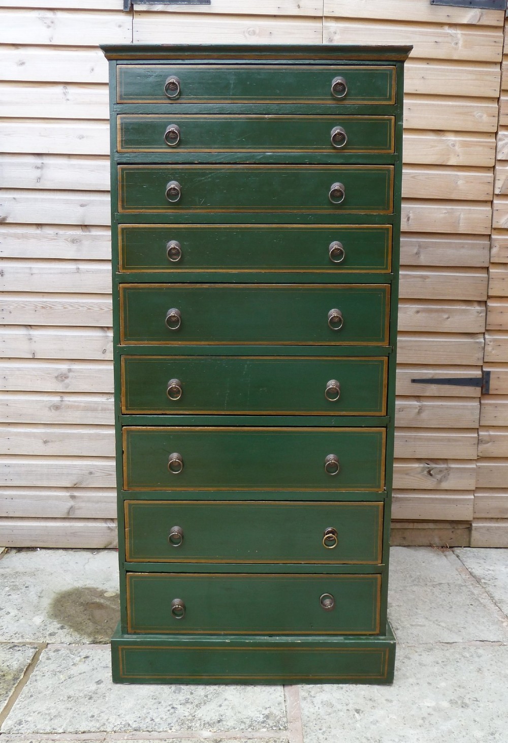 A tall dark green painted pine office chest featuring eight drawers with brass ring handles and gold pinstripe lining.