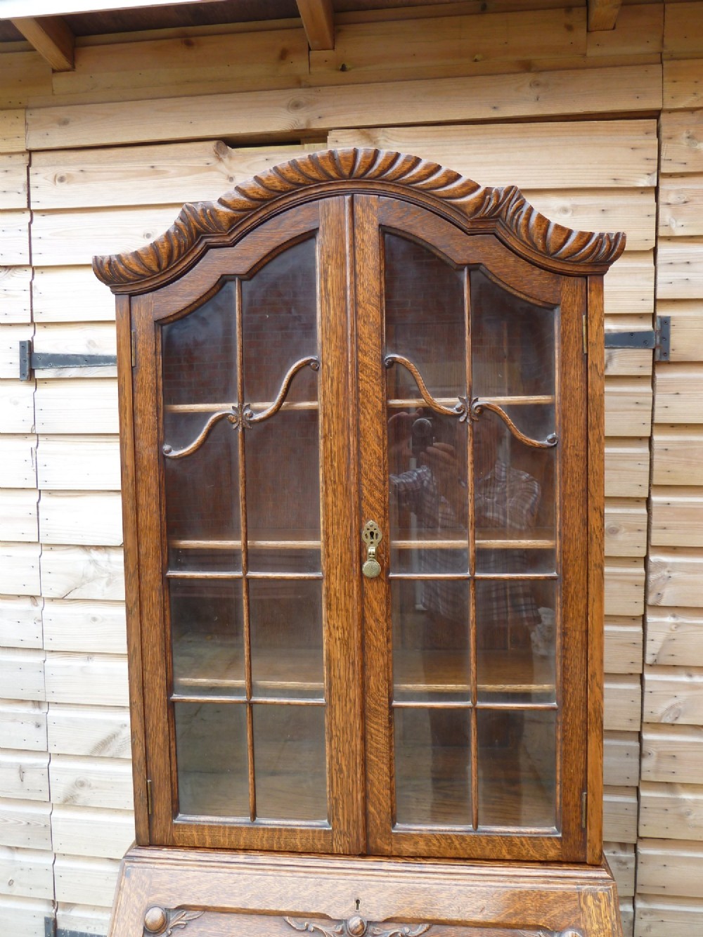 An antique oak bureau bookcase featuring an arched glazed upper cabinet, carved slant-front desk flap, drawers, and turned legs with an X-stretcher. View II