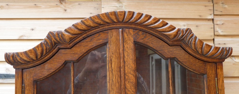 An antique oak bureau bookcase featuring an arched glazed upper cabinet, carved slant-front desk flap, drawers, and turned legs with an X-stretcher. View VIII