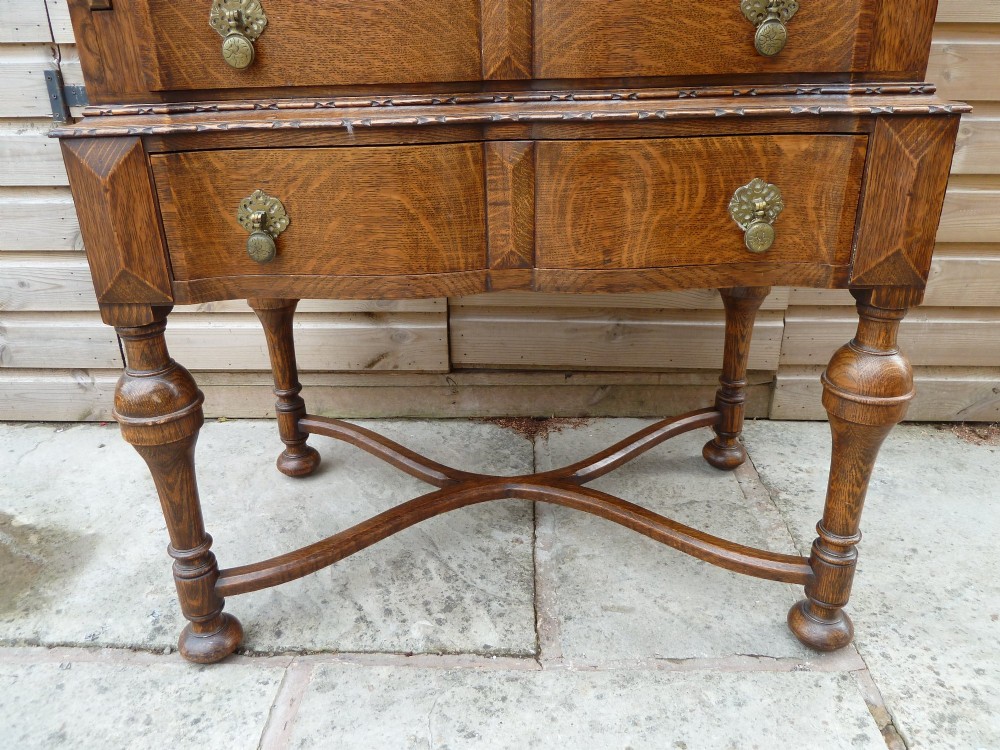 An antique oak bureau bookcase featuring an arched glazed upper cabinet, carved slant-front desk flap, drawers, and turned legs with an X-stretcher. View X