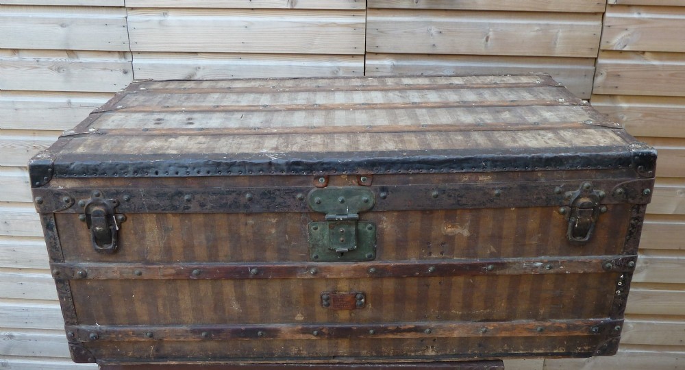 An open 19th-century flat-top steamer trunk featuring a brown striped canvas exterior, brass hardware, wood slatted bindings, and a cream quilted fabric interior lid lining. View II