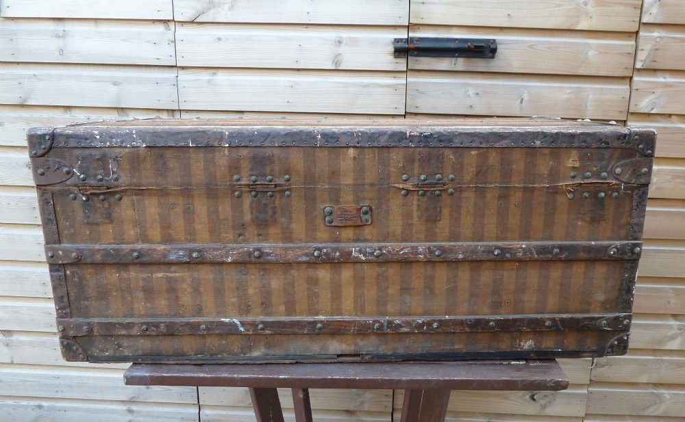 An open 19th-century flat-top steamer trunk featuring a brown striped canvas exterior, brass hardware, wood slatted bindings, and a cream quilted fabric interior lid lining. View VII