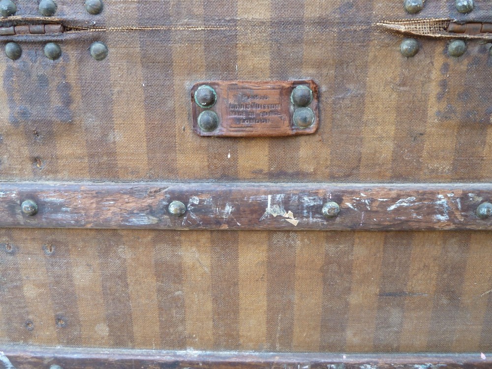 An open 19th-century flat-top steamer trunk featuring a brown striped canvas exterior, brass hardware, wood slatted bindings, and a cream quilted fabric interior lid lining. View IX