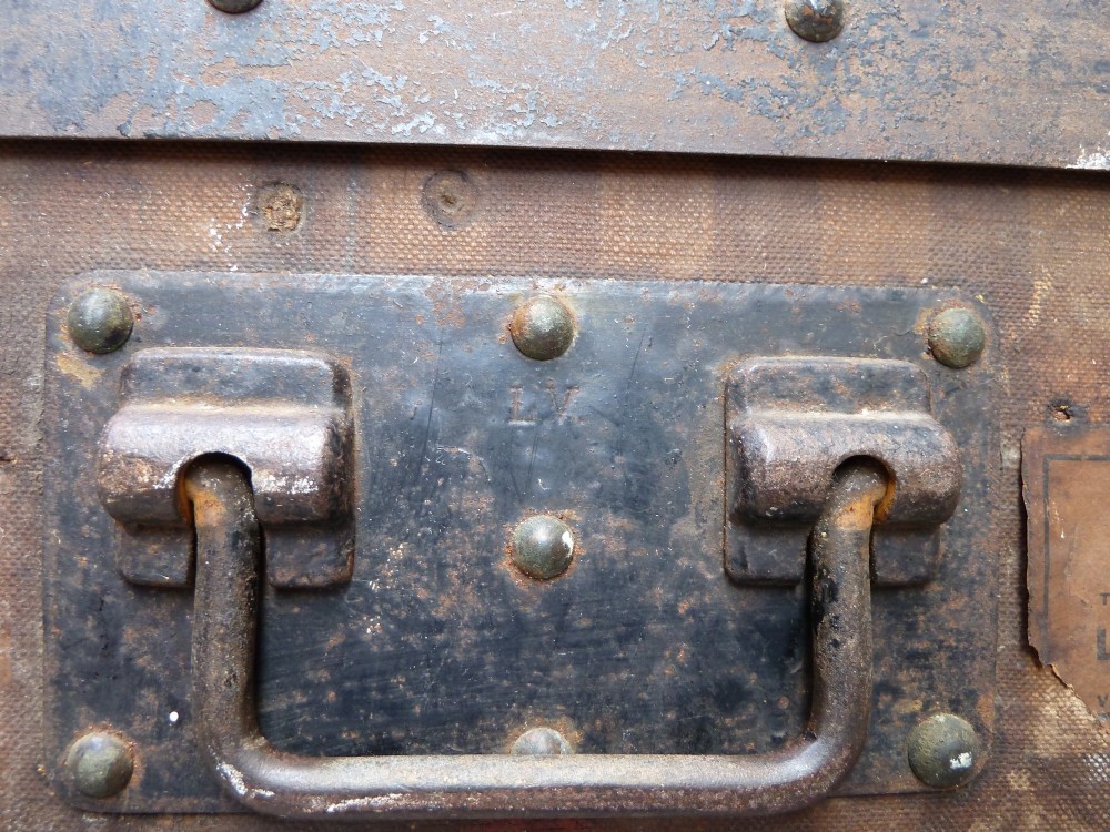 An open 19th-century flat-top steamer trunk featuring a brown striped canvas exterior, brass hardware, wood slatted bindings, and a cream quilted fabric interior lid lining. View X