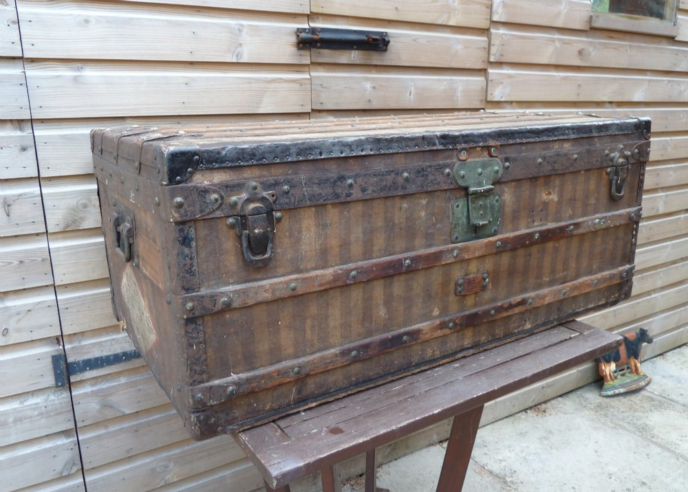 An open 19th-century flat-top steamer trunk featuring a brown striped canvas exterior, brass hardware, wood slatted bindings, and a cream quilted fabric interior lid lining. View XIV
